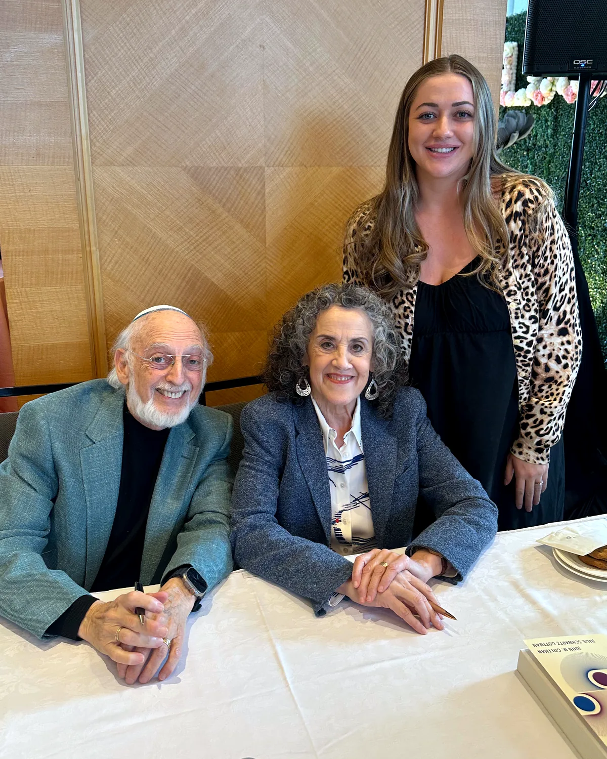 Cassandra Monroe standing behind Drs. John and Julie Gottman, who are seated at a table